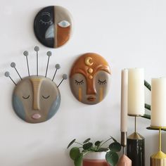 three decorative wall hangings on the wall above a table with candles and vases