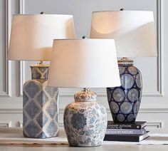 three blue and white vases sitting on top of a table next to two lamps