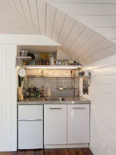 a small kitchen with white cabinets and wood flooring in an attic style space that has been converted into a studio apartment