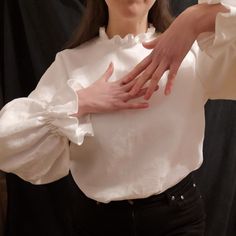 a woman in white shirt holding her hands on top of her chest and looking at the camera