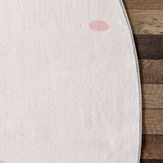 a white rug with pink polka dots on the floor next to a wooden wall and wood planks