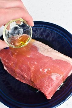 a person pouring oil on top of raw meat in a blue bowl with other food items