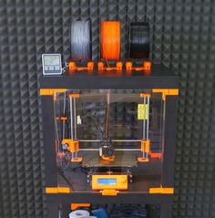 an orange and black 3d printer sitting on top of a shelf