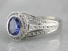 Another easy to wear ring, this one would make a spectacular engagement piece. This is 18k white gold, very well made, paved with diamonds on three sides. The center stone is Tanzanite, a bright purple oval with plenty of sparkle. Metal: 14K White Gold Gem: Tanzanite Gem Measurements: 5 x 7 mm, Oval Accents: 93 Diamonds totaling .48 Carats Ring Size: 7 Oval Sapphire Ring With Pave Setting In Platinum, Oval Tanzanite Diamond Ring In White Gold, Oval Halo Ring With Pave Setting For Anniversary, Oval White Gold Halo Ring With Pave Setting, Classic Oval Sapphire Ring With Pave Setting, Dazzling Oval Sapphire Ring With Brilliant Cut, Oval Sapphire Ring With Pave Setting, Exquisite Oval Ring With Pavé Setting, Exquisite Oval Rings With Pave Setting