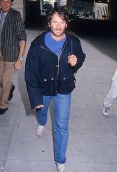 a man is walking down the sidewalk with his hand in his pocket and wearing a blue jacket