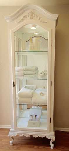 a white china cabinet with towels and candles in it's glass door display case