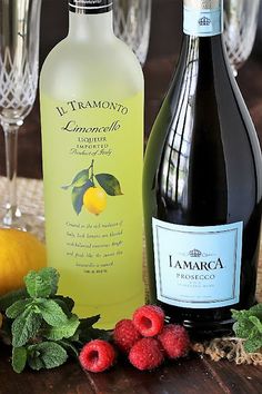 two bottles of lemonade next to some raspberries on a table with wine glasses