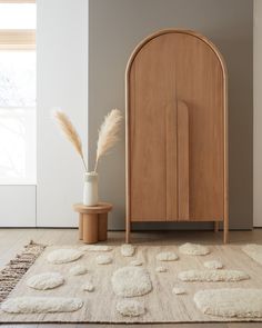 a wooden cabinet sitting on top of a rug next to a vase with dry grass in it