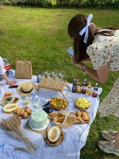 two women sitting at a picnic table with food and drinks on the grass in front of them