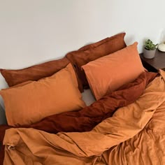 an unmade bed with orange sheets and pillows on it in a room next to a plant