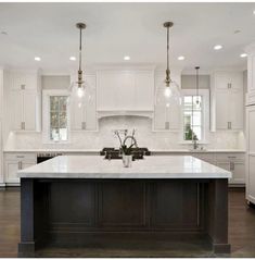 a large white kitchen with an island in the middle and two pendant lights hanging from the ceiling