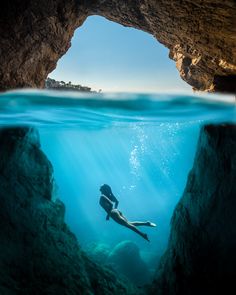 a woman swimming in the ocean near a cave with an open door to another cave