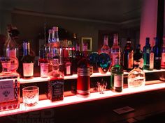 many bottles and glasses are lined up on a shelf in front of a mirror with lights