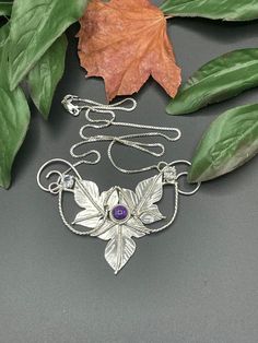 A Woodland leaves inspired necklace I've designed, entirely in sterling silver, which will feature a glowing and rich 8mm cabochon gemstone with two smaller, 4mm faceted White Topaz on either side of the main gem. This piece is approximately 3.5 inches across and I will attach a sterling silver box chain, to either end, for a total length of 18 inches when worn. If you prefer a different length, please contact me as I will adjust the chain to fit your preferences! I have offered various gemstone Silver Mystical Necklace With Cabochon, Hand Forged Silver Necklaces In Nature-inspired Style, Handmade Sterling Silver Leaf Necklace, Hand Forged Silver Nature-inspired Necklace, Hand-forged Silver Nature-inspired Necklace, Silver Amethyst Cabochon Necklace, Silver Amethyst Necklace With Cabochon, Nature-inspired Sterling Silver Necklaces With Unique Variations, Bohemian Sterling Silver Cabochon Necklaces