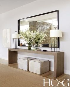 a large mirror sitting above a table with two stools and a vase filled with flowers