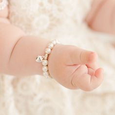 Baby girl wearing the white luster pearl bracelet around her wrist, part of our baby jewelry collection. Silver Heart-shaped Pearl Bracelet For Gift, Pearl Heart Bracelet With Charm, Pearl Heart Bracelet For Wedding, Elegant Pearl Bracelet With Heart Beads For Wedding, Wedding Pearl Heart Bracelet, Wedding Heart-shaped Pearl Bracelet, Adjustable Pearl Heart Bracelet, White Pearl Bracelet With Heart Charm For Wedding, Elegant Pearl Heart Bracelet With Heart Beads