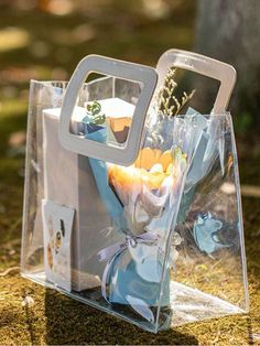 a clear bag with flowers in it sitting on the ground next to a tree and grass