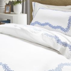 a bed with white and blue comforters in a bedroom next to a night stand