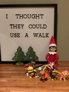 an elf is standing next to some toys on a table with a sign in the background