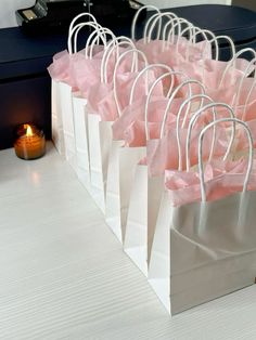 small white bags with pink tissue paper are lined up on a table next to a candle