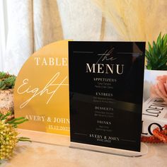 a table sign sitting on top of a table next to a vase with flowers and succulents