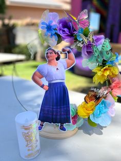 a paper cut out of a woman with flowers and butterflies on her head, next to a candle