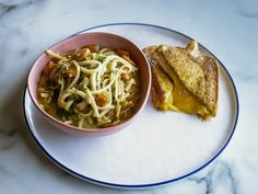 a white plate topped with a bowl of food next to a slice of toast on top of a table