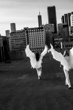 two people dressed in white are dancing with their arms spread out and buildings in the background