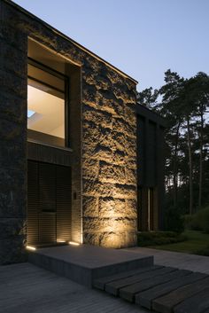 an exterior view of a modern house with stone walls and steps lit up at night