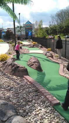 two children playing miniature golf at the miniature golf course in an amusement park with rocks and grass