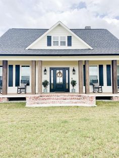 a white house with black shutters on the front porch and two chairs in front