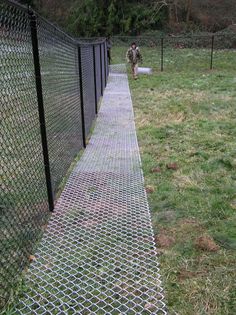 a man walking down a path next to a fence with an arrow sign on it