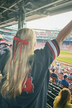 a woman with long blonde hair standing at a baseball game