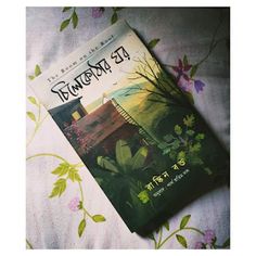 a book sitting on top of a bed covered in green leaves and flowers next to a pillow