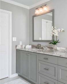 a large bathroom with gray cabinets and marble counter tops, white flowers in vase on the sink