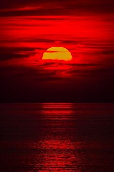 the sun is setting over the ocean with red clouds