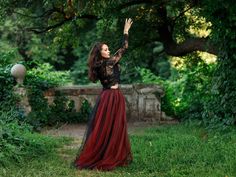 a woman in a red and black dress is standing under a tree with her hands up