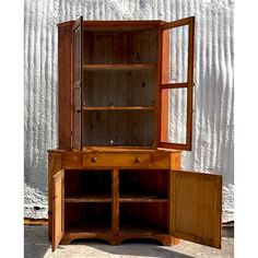 an old wooden cabinet with glass doors and drawers in front of a white wall behind it