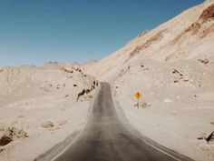 an empty road in the middle of desert with no traffic sign on one side and mountains in the background