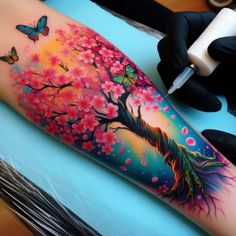 a woman's arm with a colorful tree and butterflies on it, while she is getting her tattoo done