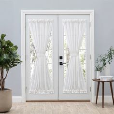 a white door with curtains and a potted plant on the side table next to it