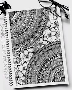 a spiral notebook with an intricate design on the cover and some reading glasses next to it