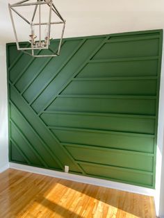 an empty room with a green wall and wooden flooring in the center is a light fixture