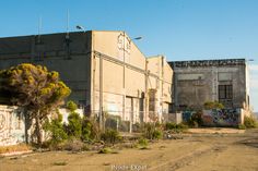 an old building with graffiti on it and trees in the foreground, next to a dirt road