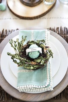 a place setting with green napkins and an egg in a nest on the plate