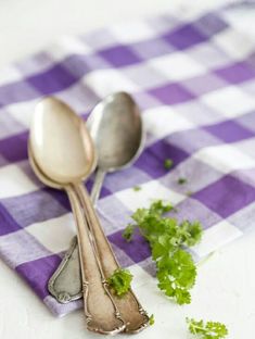 two spoons sitting on top of a purple and white checkered table cloth with parsley