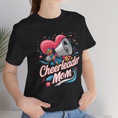 Show your school spirit with our **Cheer Mom Shirt Perfect for supporting your cheerleader, this **Cheerleader Mom Shirt** is designed for proud moms who love to cheer on their kids. This **Cheer Mom Tee** is great for game days, competitions, and school events. It makes an excellent **Cheer Mom Gift** and is a must-have addition to any cheer mom's wardrobe. Whether you're in the stands or on the go, this **School Spirit Tshirt** will showcase your pride and enthusiasm. Our **Cheer Spirit Wear** is made with comfort and style in mind, ensuring you look great while rooting for your team. Get ready to shine with this versatile **Cheer Tee **Product Details - 100% Airlume combed and ringspun cotton (fiber content may vary for different colors) - Light fabric (4.2 oz/yd² (142 g/m - Retail fit Graphic Tee T-shirt For Cheerleading, Team Spirit Tops With Sublimation Print For Cheerleading, Cheerleading Fan Apparel Tops With Sublimation Print, Cheerleading Graphic Print Fan Apparel Tops, Sports Fan T-shirt With Team Name For Cheerleading, Crew Neck T-shirt With Sublimation Print For Cheerleading, Cotton T-shirt For Cheerleading In Fan Apparel Style, Cotton T-shirt For Cheerleading Fan Apparel, Black T-shirt For Cheerleading Fan Apparel