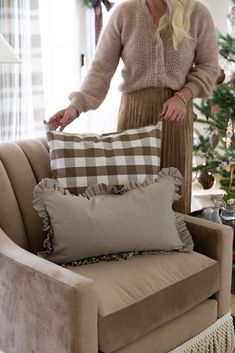 a woman standing in front of a couch with pillows on it and a christmas tree behind her