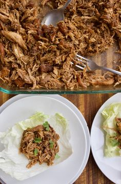 two white plates topped with lettuce next to a casserole dish filled with shredded meat