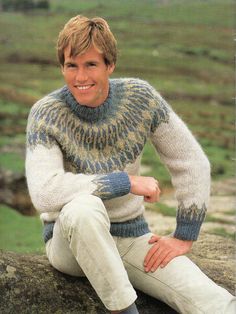 a man sitting on top of a rock wearing a sweater